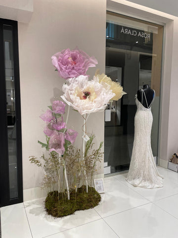 Arreglo de flores gigantes de papel sobre base de musgo junto a un maniqui con vestido de novia