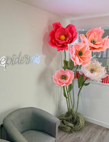 Flores decorativas gigantes de papel en tonos rosa junto al letrero de pared epidermis
