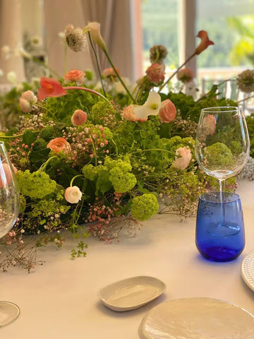 Centro de mesa con flores variadas y copas de cristal sobre una mesa blanca
