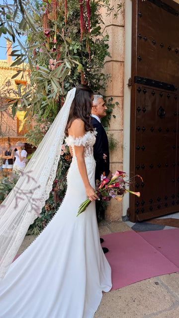 Novia con vestido blanco y velo largo caminando junto a un hombre hacia la entrada de una iglesia