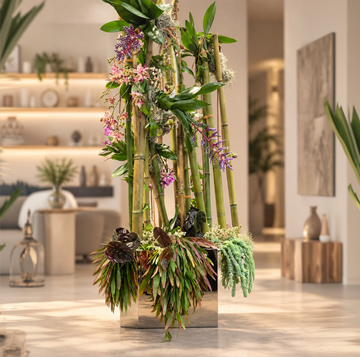 Arreglo floral con tallos de bambú y plantas verdes en maceta metálica cuadrada