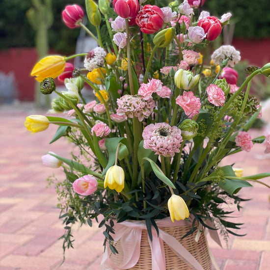 Jardín de Alegría — cesta de mimbre con tulipanes, claveles rosas y cinta de tul