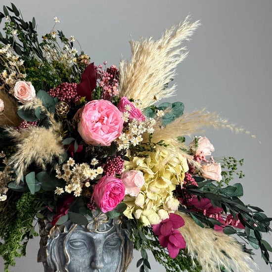 Jarrón escultórico con rostro y arreglo floral de rosas y plumas de pampas