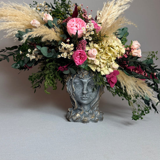 Jarrón de rostro con rosas rosas y hortensia sobre superficie gris