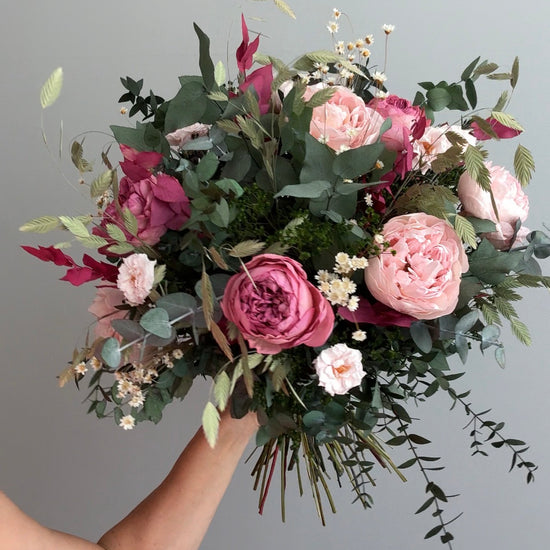 Mano levantando ramo de rosas rosas y burdeos con eucalipto colgante