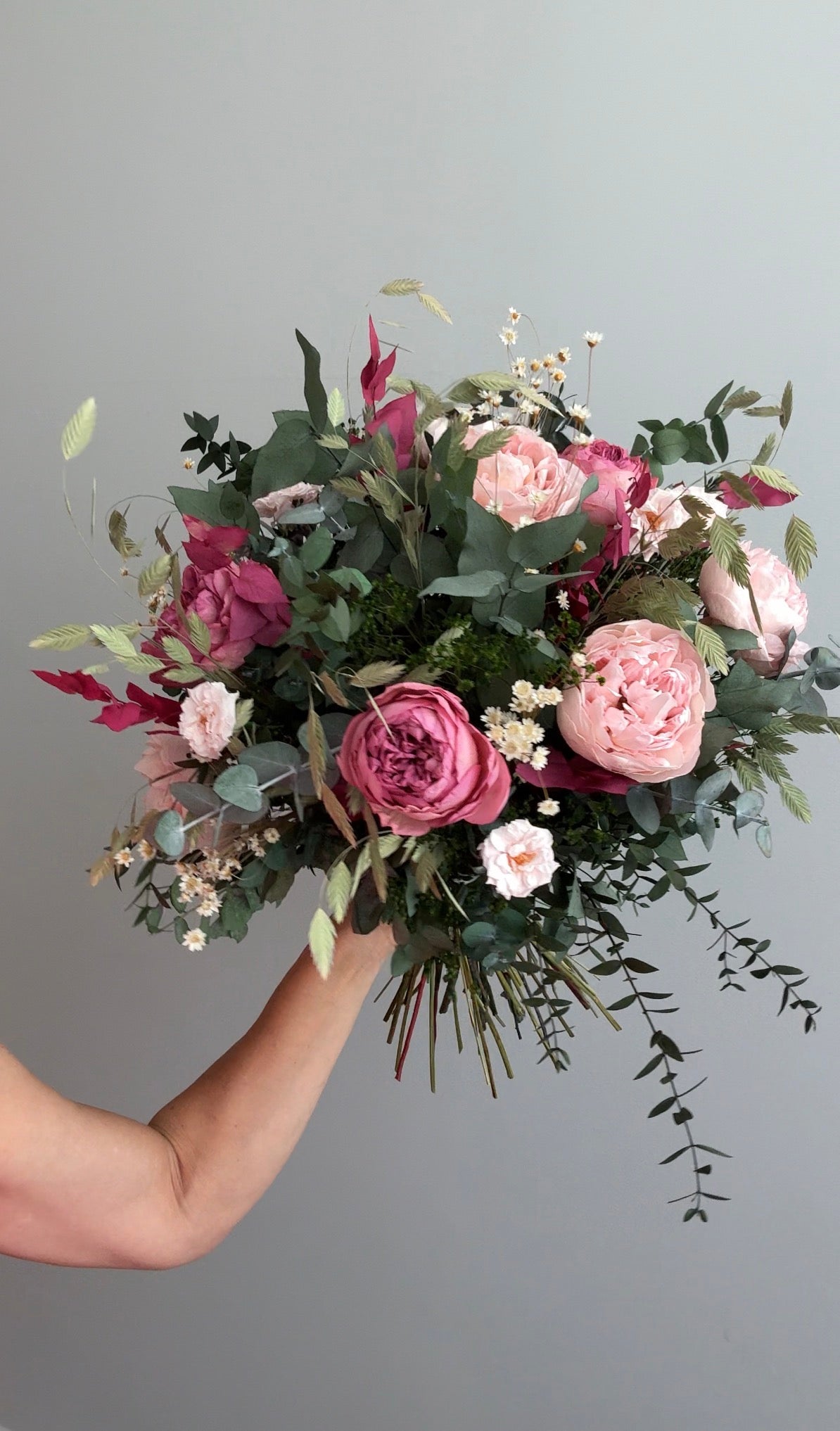 Mano levantando ramo de rosas rosas y burdeos con eucalipto colgante