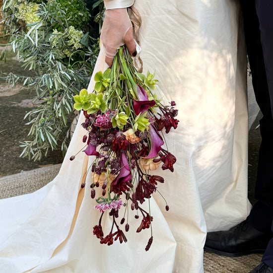 Novia sosteniendo ramo con calas moradas junto al novio, estilo colgante