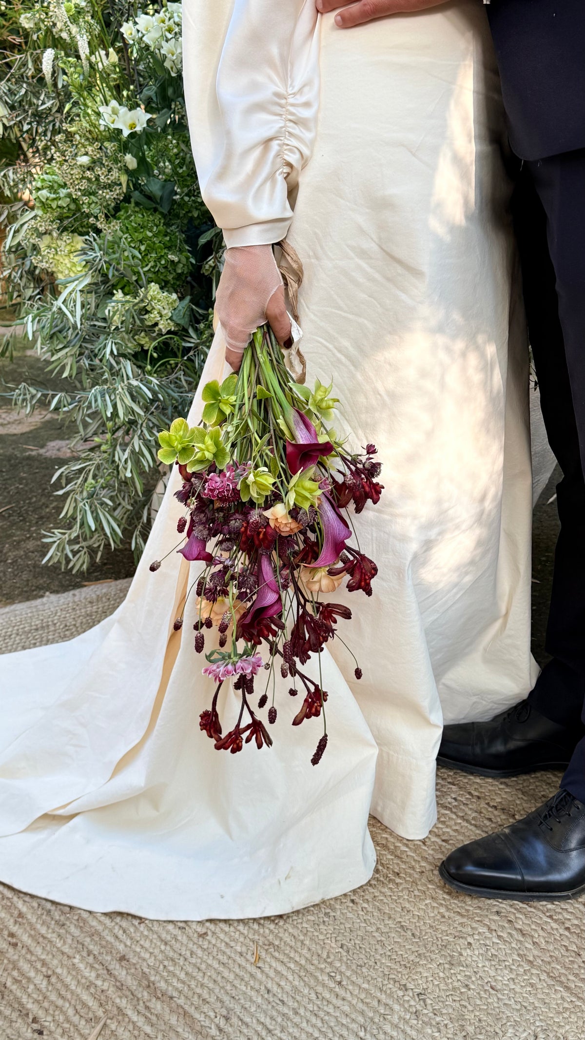 Novia sosteniendo ramo con calas moradas junto al novio, estilo colgante
