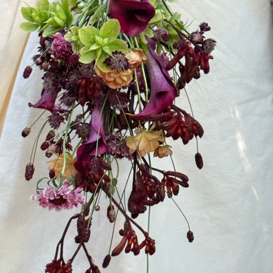 Novia con ramo de calas moradas y flores otoñales junto al vestido