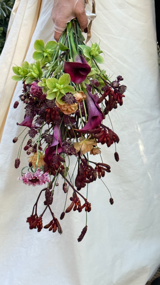 Novia con ramo de calas moradas y flores otoñales junto al vestido