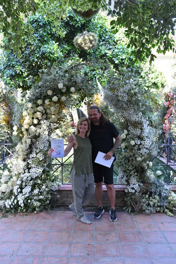 Pareja bajo arco floral blanco de rosas y margaritas en jardín