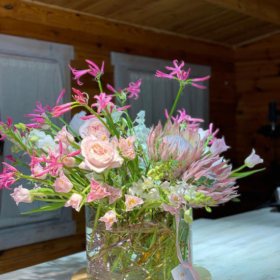 Pink Reverie — composición con protea rosa, cymbidium y rosas en jarrón, etiqueta ANHUÁ