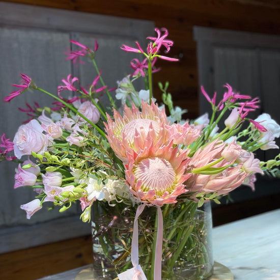 Pink Reverie — primer plano de protea rosa en jarrón con nerina fucsia