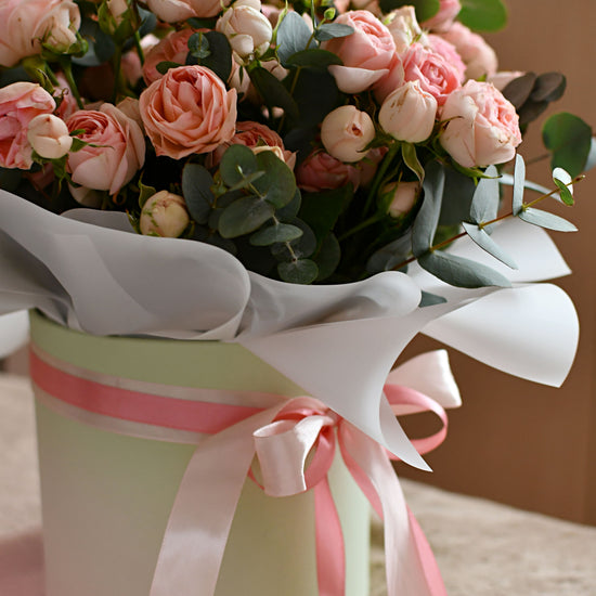 Bouquet of pink and peach roses with eucalyptus in a pastel green gift box decorated with pink ribbons