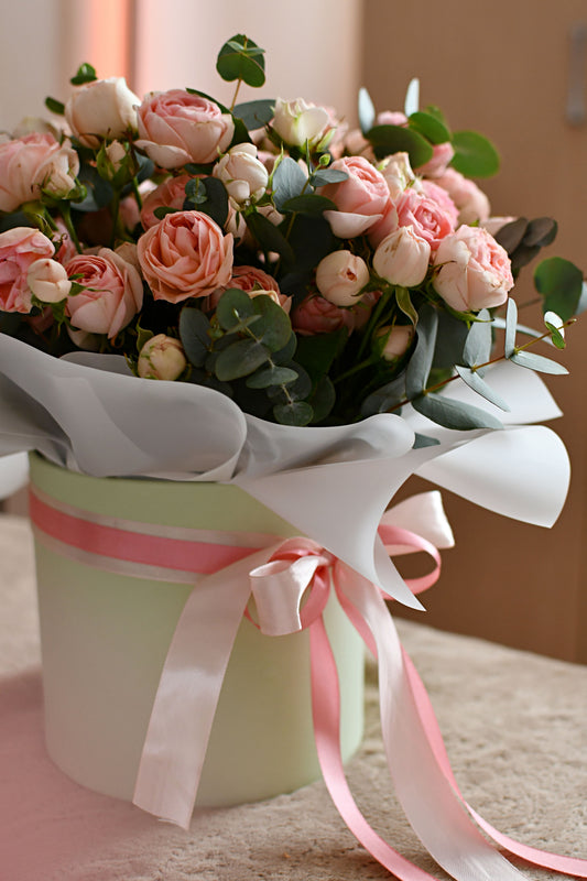 Bouquet of pink and peach roses with eucalyptus in a pastel green gift box decorated with pink ribbons