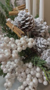 Composición navideña con piñas nevadas, canela, bayas perladas, verdes de abeto y velas blancas