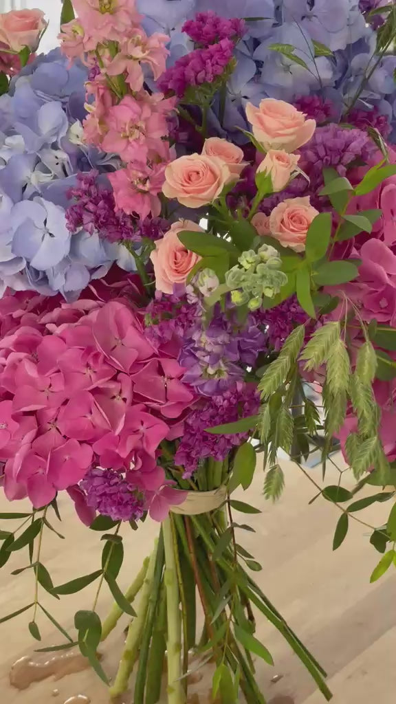 Vídeo de detalle del ramo con hortensias lilas y rosas, mini rosas melocotón, delphinium y limonium morado