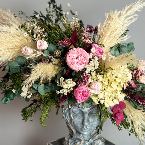 Primer plano de arreglo floral con rosas rosas, hortensia y plumas de pampas
