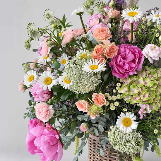 Arreglo floral variado con peonías rosas margaritas y hortensias en una cesta de mimbre sobre fondo gris