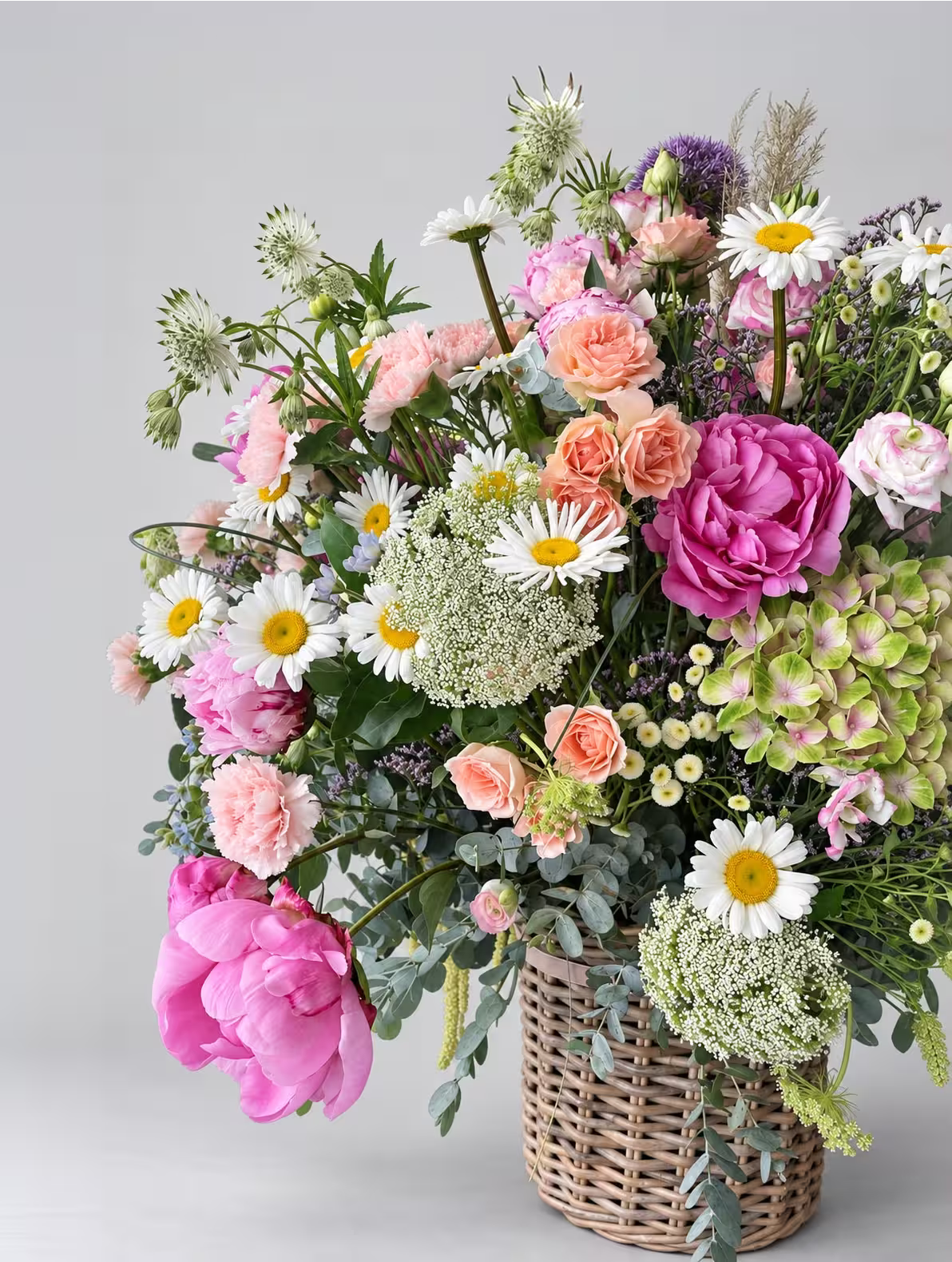 Arreglo floral variado con peonías rosas margaritas y hortensias en una cesta de mimbre sobre fondo gris