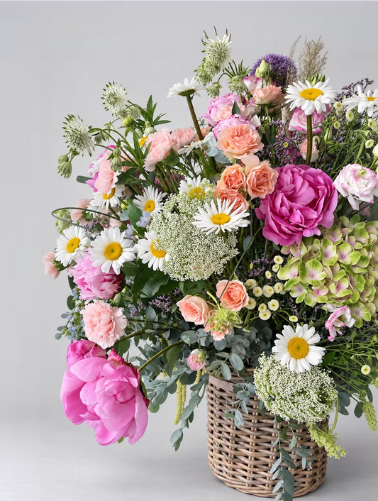 Arreglo floral variado con peonías rosas margaritas y hortensias en una cesta de mimbre sobre fondo gris