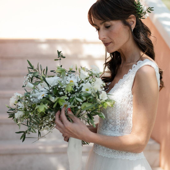 Novia con vestido de encaje sosteniendo un ramo de novia silvestre de margaritas, eustoma y olivo