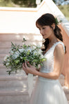 Novia con vestido de encaje sosteniendo un ramo de novia silvestre de margaritas, eustoma y olivo