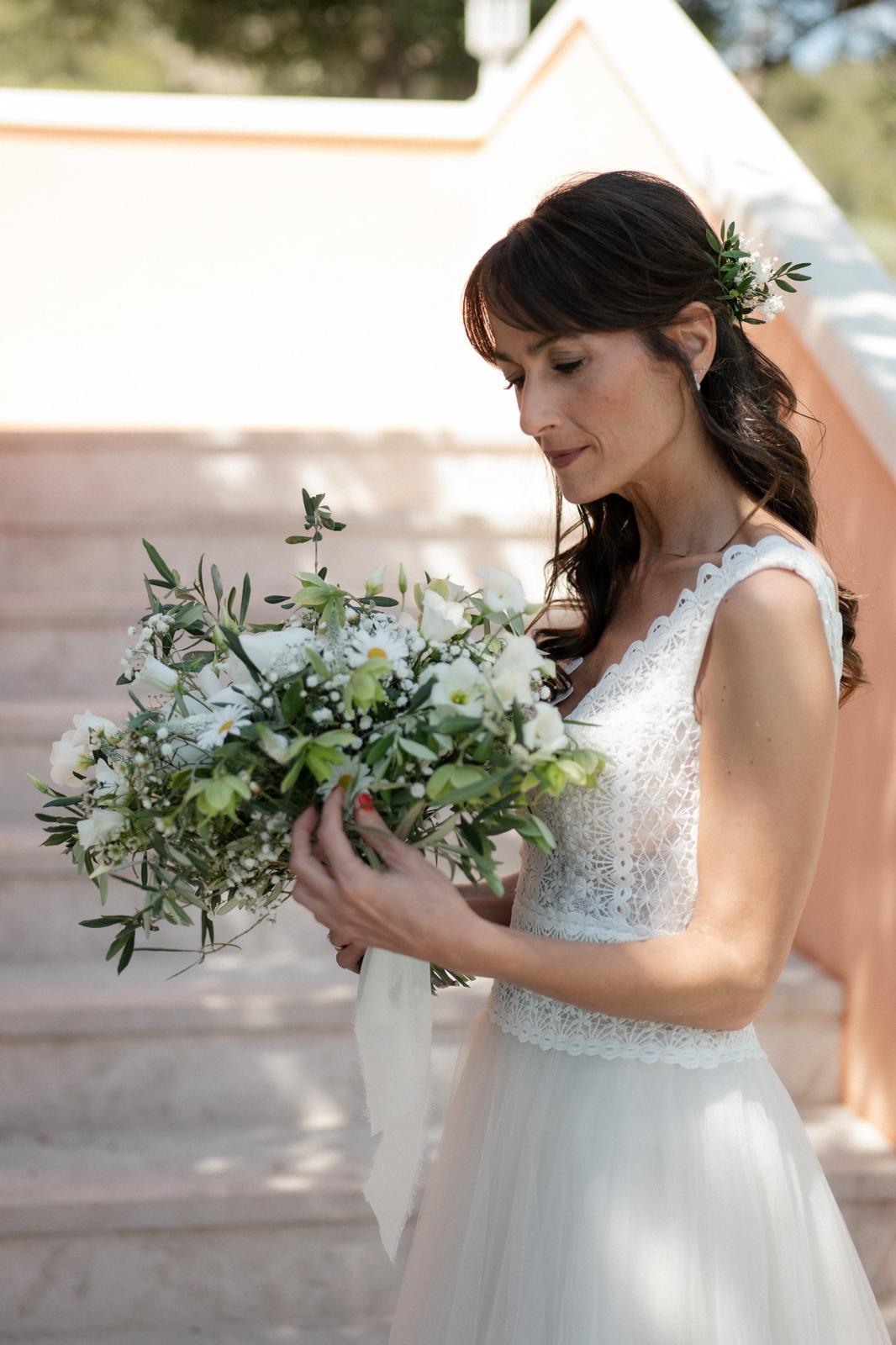 Novia con vestido de encaje sosteniendo un ramo de novia silvestre de margaritas, eustoma y olivo