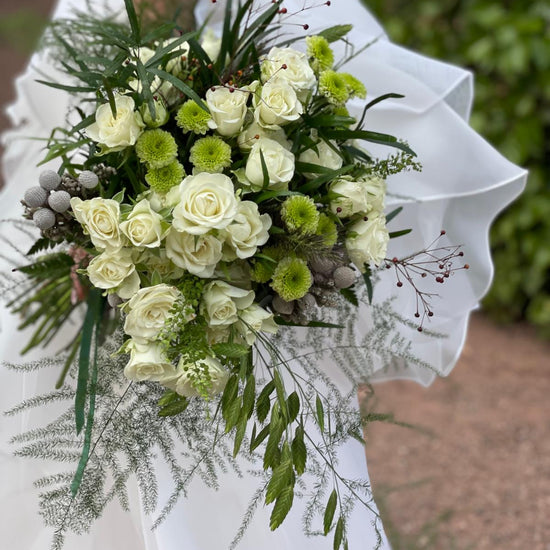 Novia con vestido de volantes sosteniendo un ramo de rosas blancas, crisantemos verdes y brunia