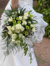 Novia con vestido de volantes sosteniendo un ramo de rosas blancas, crisantemos verdes y brunia