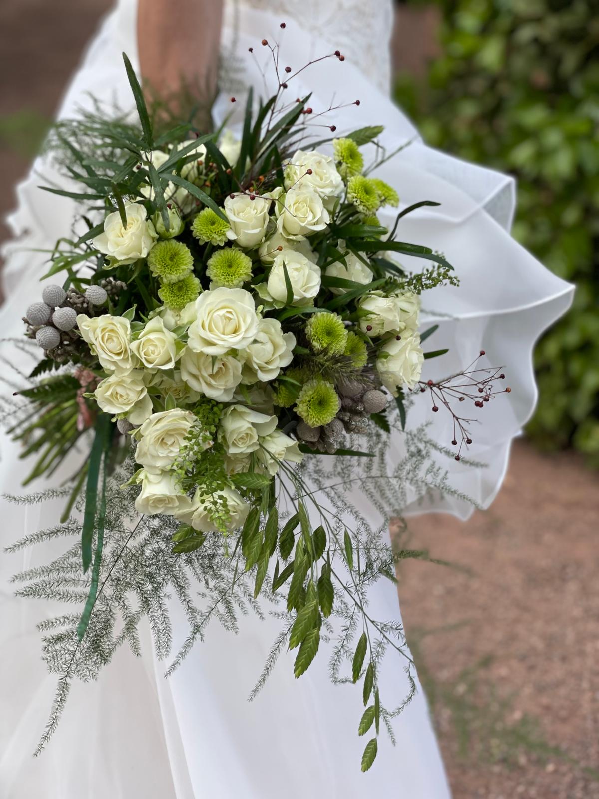 Novia con vestido de volantes sosteniendo un ramo de rosas blancas, crisantemos verdes y brunia