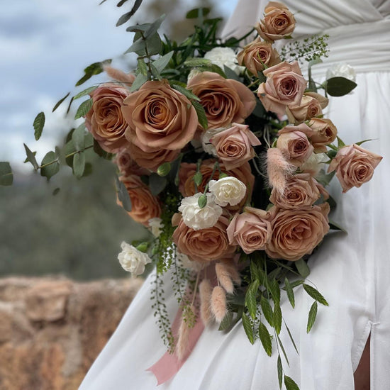 Ramo de novia con rosas color capuchino, claveles blancos, lagurus y eucalipto sobre vestido blanco