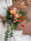 Vista lateral de ramo de novia con rosas melocotón, tulipanes rojos, esparraguera y eucalipto colgante