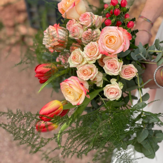 Vista superior de ramo de novia con rosas melocotón, tulipanes rojos, hypericum rojo y esparraguera
