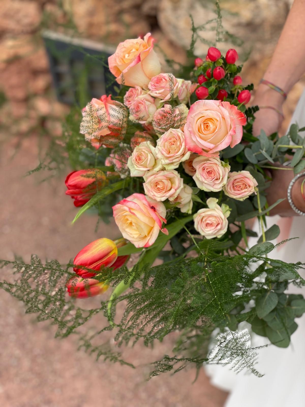 Vista superior de ramo de novia con rosas melocotón, tulipanes rojos, hypericum rojo y esparraguera