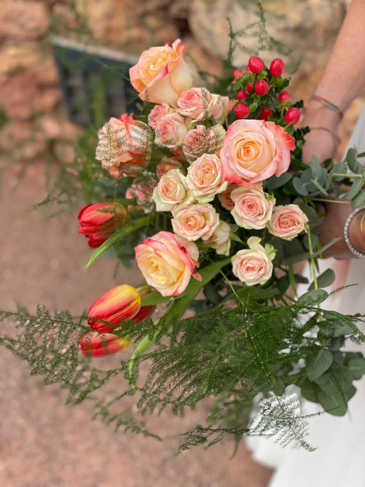 Vista superior de ramo de novia con rosas melocotón, tulipanes rojos, hypericum rojo y esparraguera