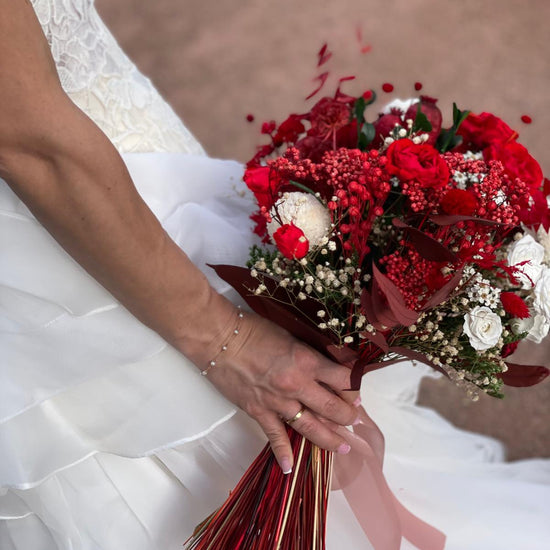 Novia sosteniendo ramo de rosas rojas y flores blancas atado con cinta rosa y tallos decorativos