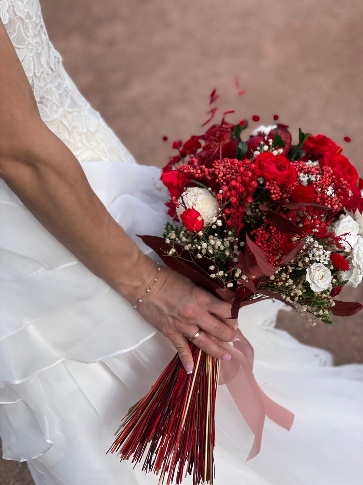 Novia sosteniendo ramo de rosas rojas y flores blancas atado con cinta rosa y tallos decorativos
