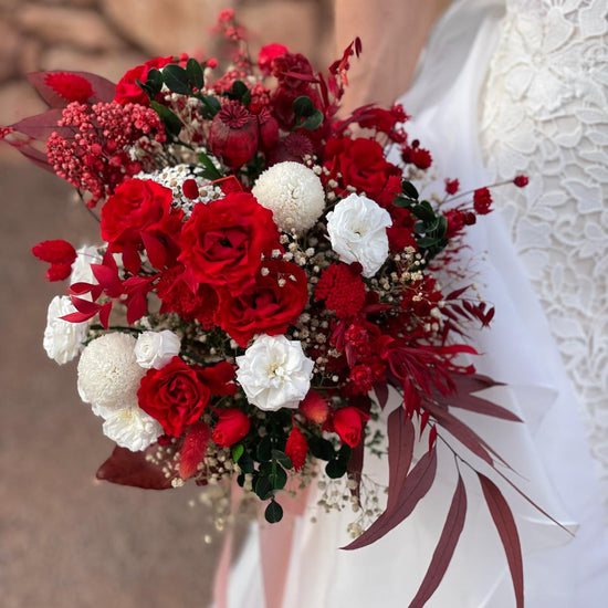 Novia con vestido blanco sosteniendo un ramo de novia con rosas rojas y flores blancas