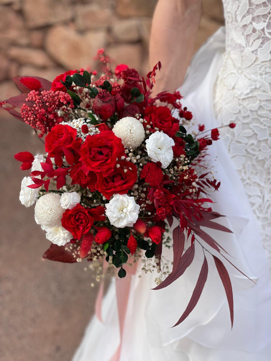 Novia con vestido blanco sosteniendo un ramo de novia con rosas rojas y flores blancas