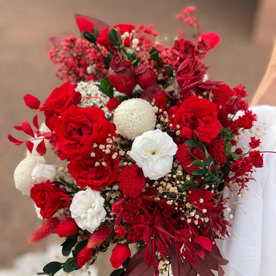 Novia sosteniendo ramo de rosas rojas y flores blancas con follaje preservado burdeos