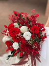 Novia sosteniendo ramo de rosas rojas y flores blancas con follaje preservado burdeos