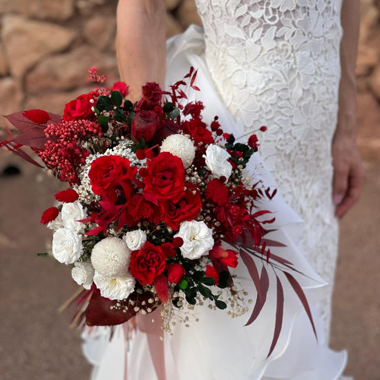 Novia con vestido de encaje blanco sosteniendo un ramo de rosas rojas y flores blancas