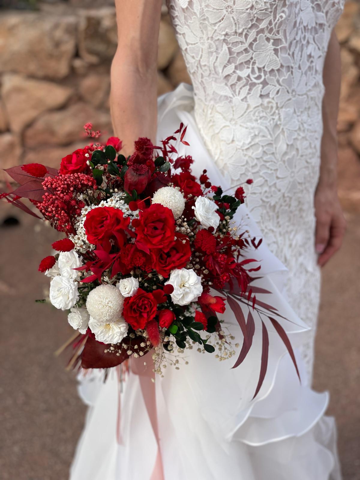 Novia con vestido de encaje blanco sosteniendo un ramo de rosas rojas y flores blancas