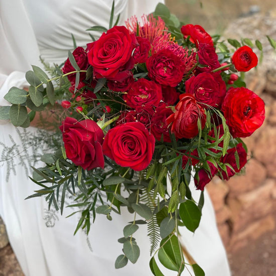 Novia con vestido blanco sosteniendo un ramo de rosas rojas y follaje verde