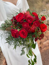 Novia con vestido blanco sosteniendo un ramo de rosas rojas y follaje verde