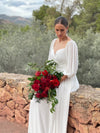 Novia sentada sobre un muro de piedra con ramo de novia de rosas rojas, leucospermum y eucalipto