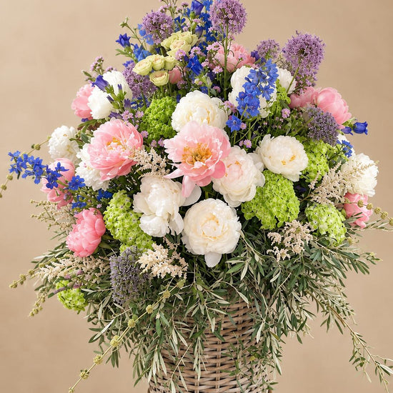 Ramo floral en cesta de mimbre con peonías, allium morado y hortensia verde sobre fondo neutro