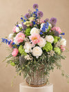 Ramo floral en cesta de mimbre con peonías, allium morado y hortensia verde sobre fondo neutro