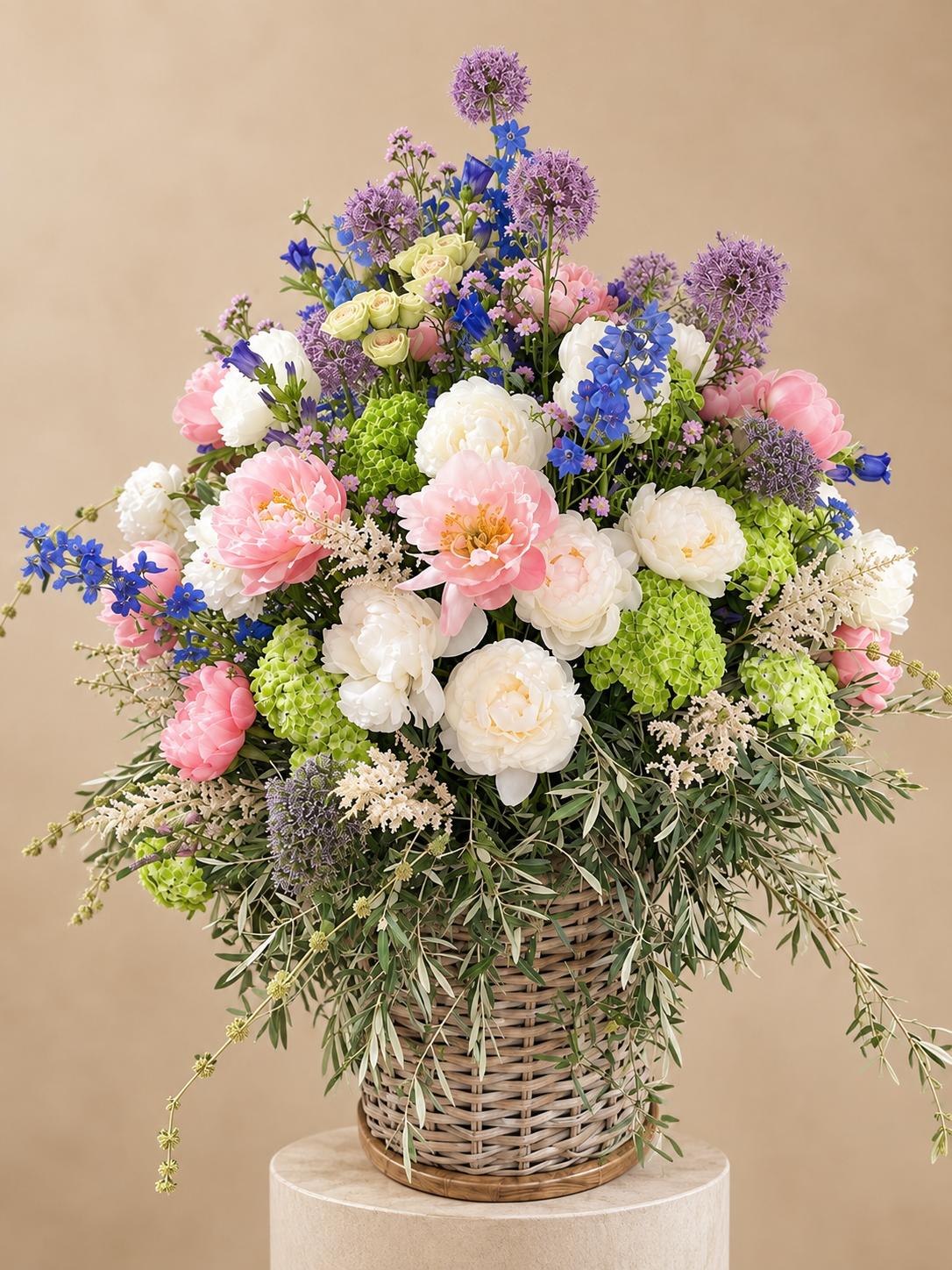 Ramo floral en cesta de mimbre con peonías, allium morado y hortensia verde sobre fondo neutro